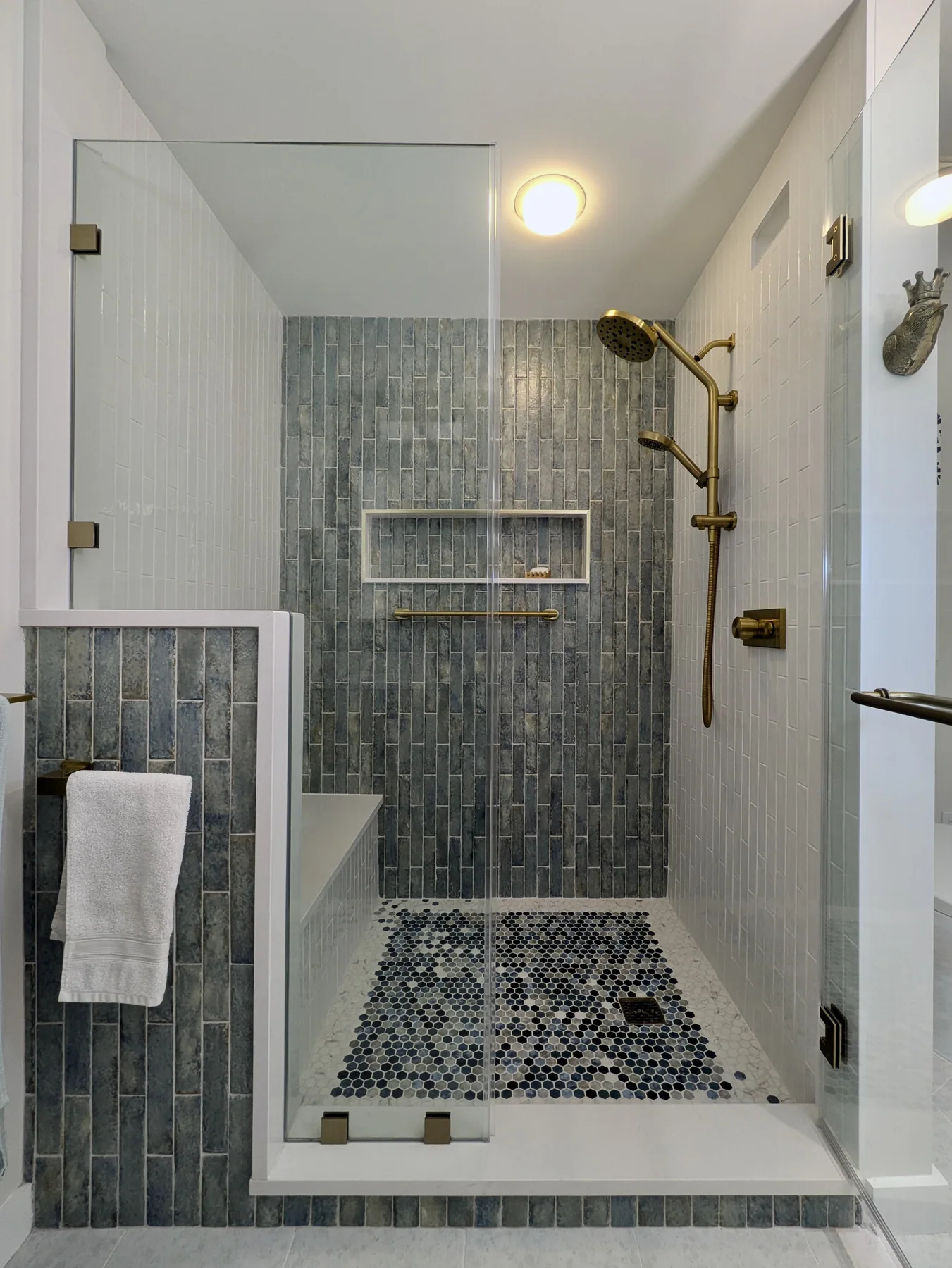 Glass shower with blue tile, brass fixtures and a mosaic tile floor