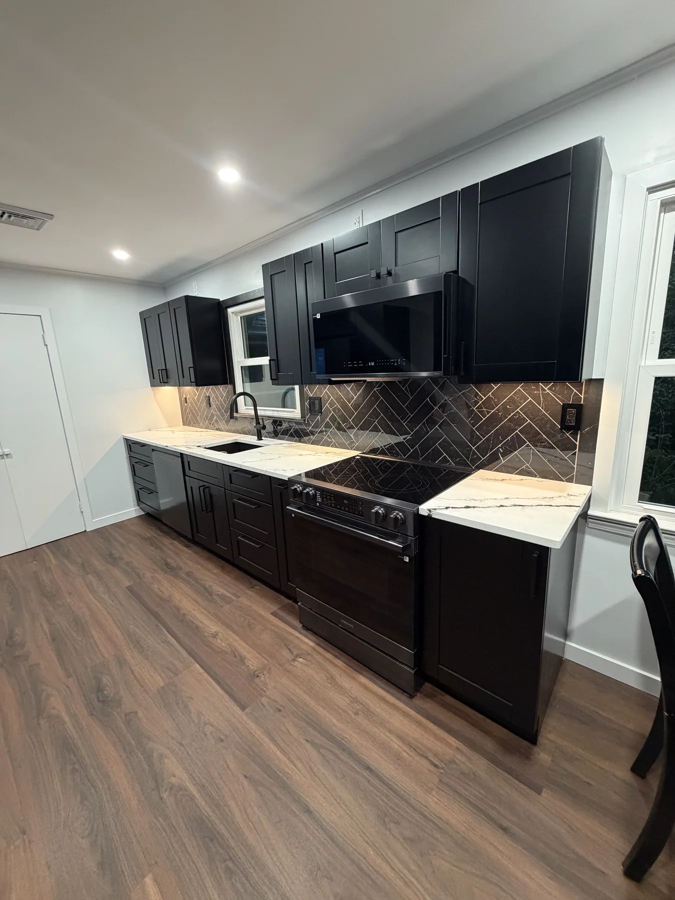 Kitchen with dark cabinetry, light countertops, herringbone backsplash and wood-look flooring