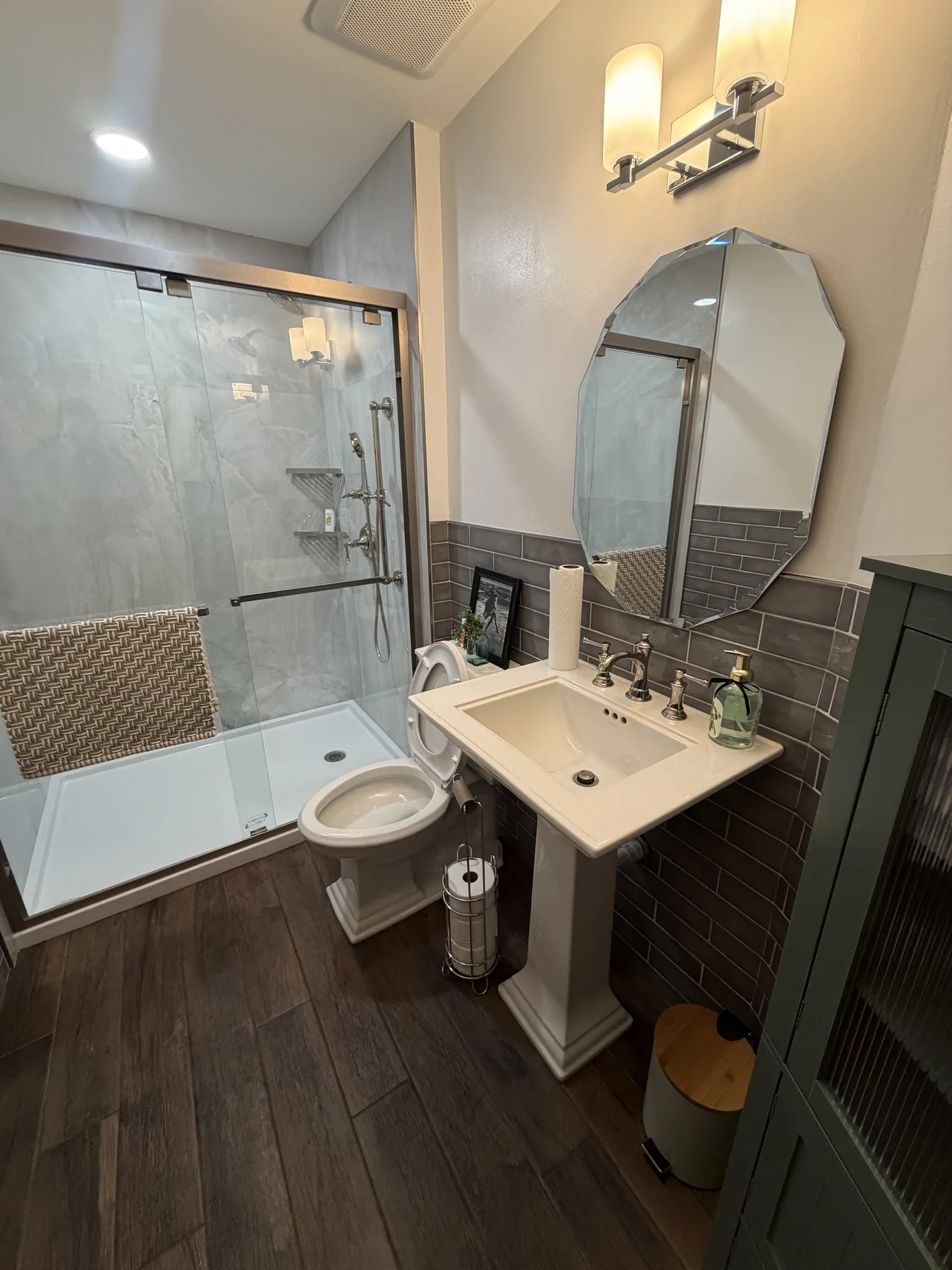 Bathroom with a white pedestal sink, beveled mirror and glass shower
