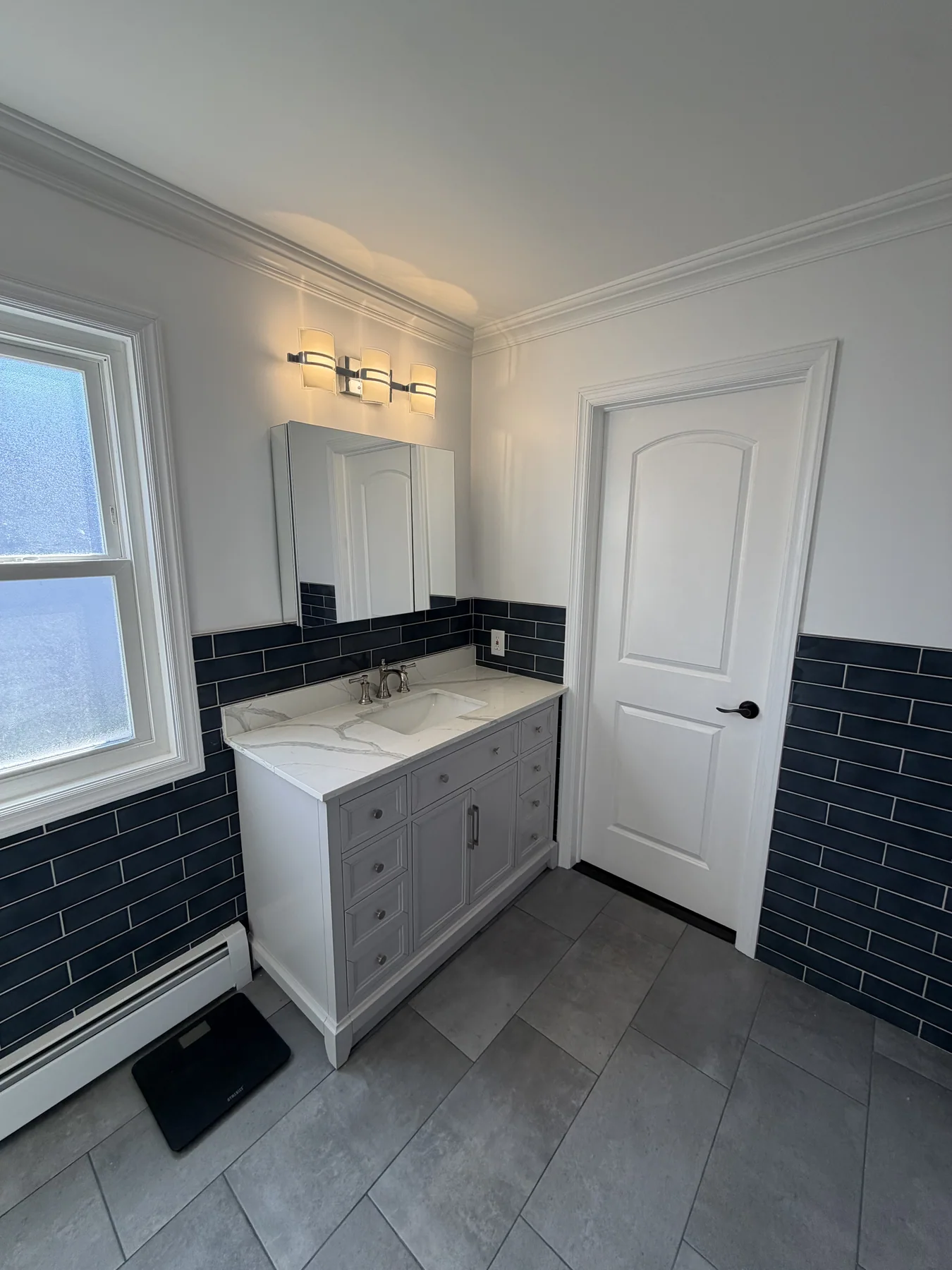 Bathroom vanity with a white countertop, navy tile wainscoting and large mirror