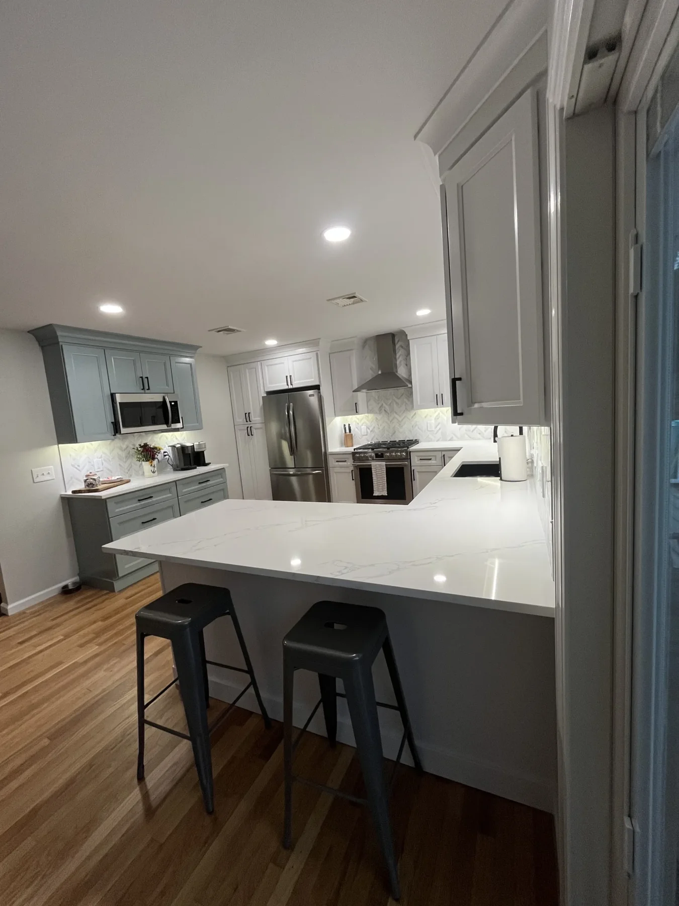 White and gray kitchen cabinetry with a white breakfast peninsula, black stools and stainless steel appliances